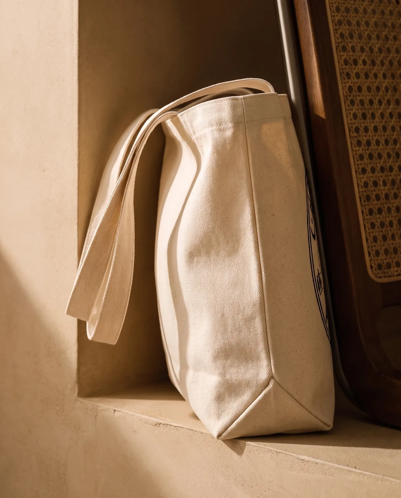 The tote in profile against a wall, the gusset folded out and the straps laid over the side